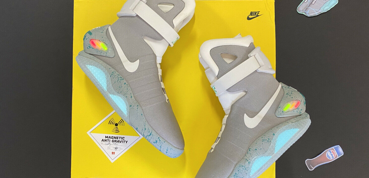 Серые кроссовки Nike Air Mag с подсветкой и ремнями, лежат на жёлтой коробке Nike