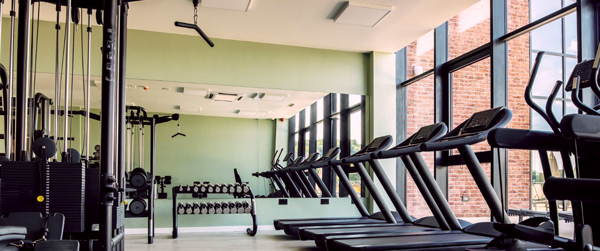 Тренажерный зал, слева тренажеры, справа панорамные окна и беговые дорожки